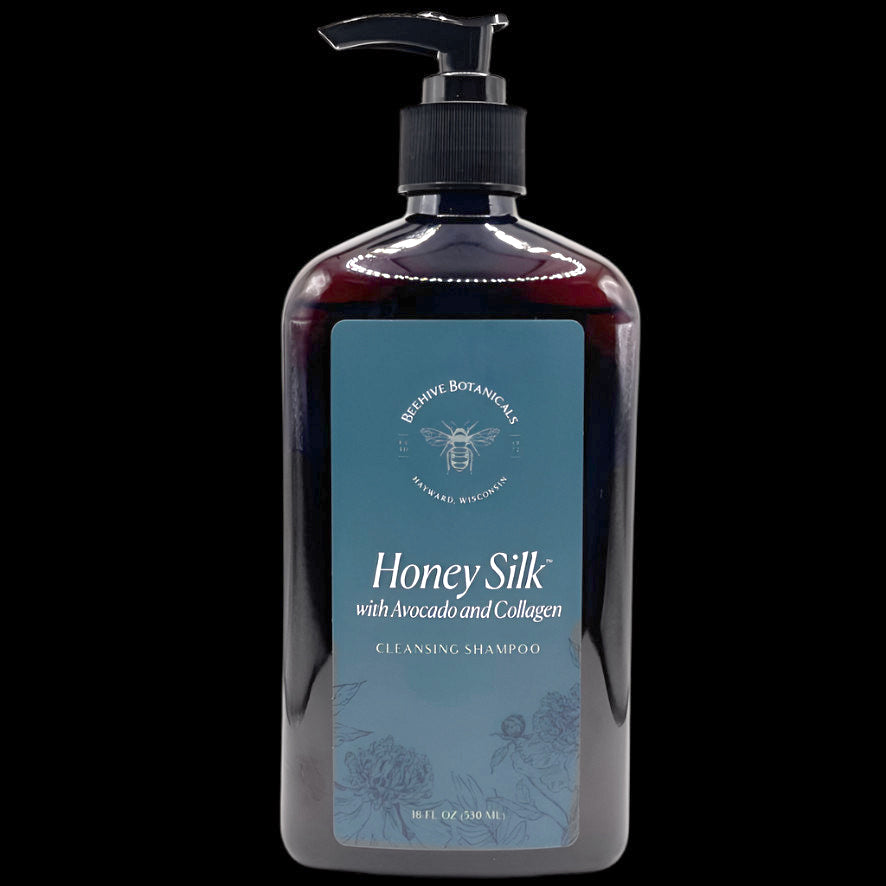 Image is of a Large, dark brown plastic bottle with a black pump and blue matte label containing white text reading "Honey Silk with Avocado and Collagen Cleansing Shampoo. 