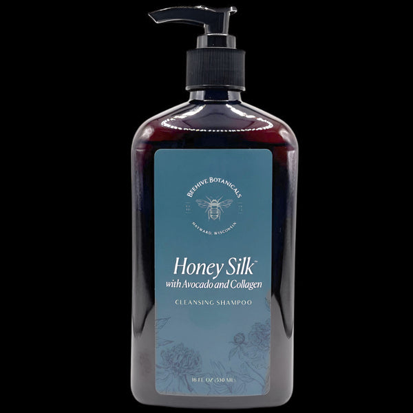 Image is of a Large, dark brown plastic bottle with a black pump and blue matte label containing white text reading "Honey Silk with Avocado and Collagen Cleansing Shampoo. 