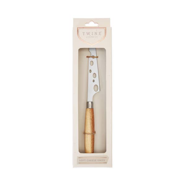 Image of Acacia Wood handled soft cheese knife with stainless steel blade containing aesthetically designed oval perforations viewable through the package window of a tan box with the 'Twine' logo printed at the top. 