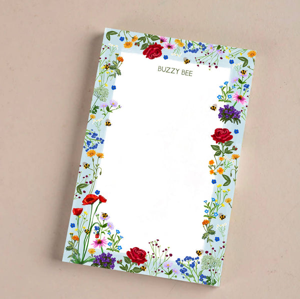 Accessories & Crocks - Bee And Flower Notepad for Higbee Honey with blue and floral elements border with bees . Notepad is on a beige background. Paper and accessories.