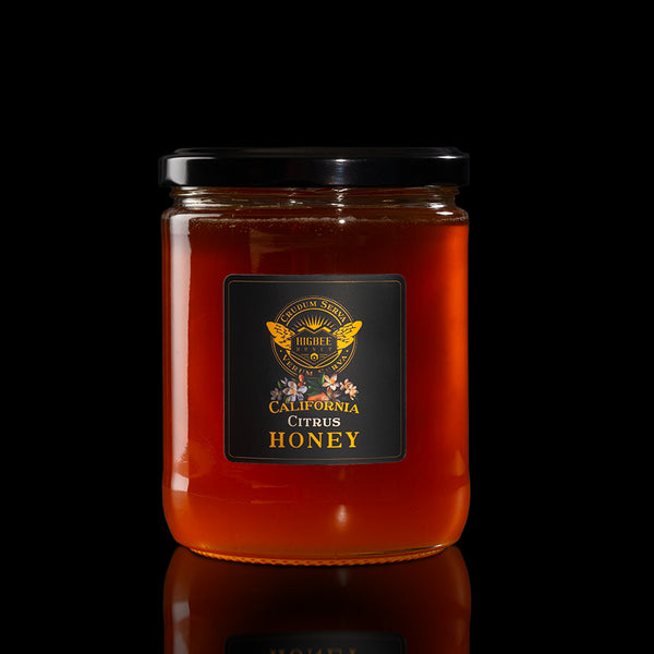 Higbee Honey - Southern California Raw Unfiltered Citrus Honey Honey -  in a 20z. Jar with a black lid and black and gold label with Citus floral elements in front of a seal of Higbee Honey that includes the Higbee Honey Logo. Jar is on a glossy surface with reflection of the jar and everything is on a black background.