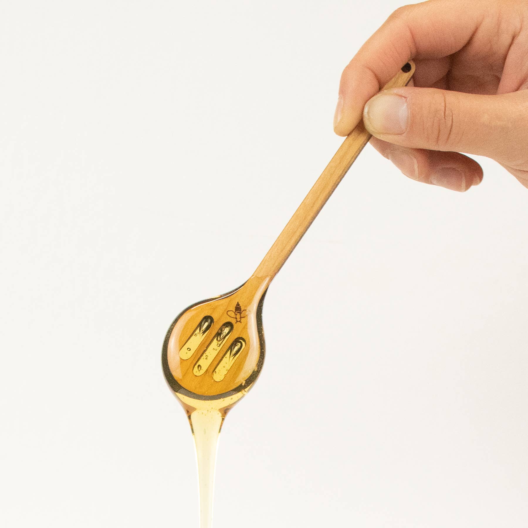 Higbee Honey laser Cut Honey dipper 1a held by a hand with honey drizzling on a white background